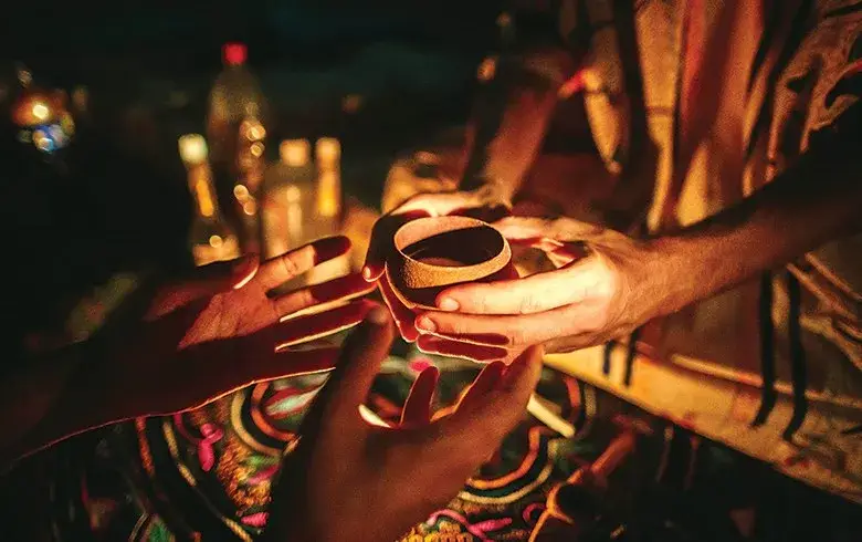 Mãos entregando uma cuia com ayahuasca à luz de velas