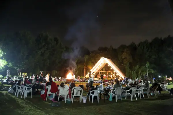 Ritual noturno ao ar livre, com participantes em círculo, fogueira e o templo iluminado